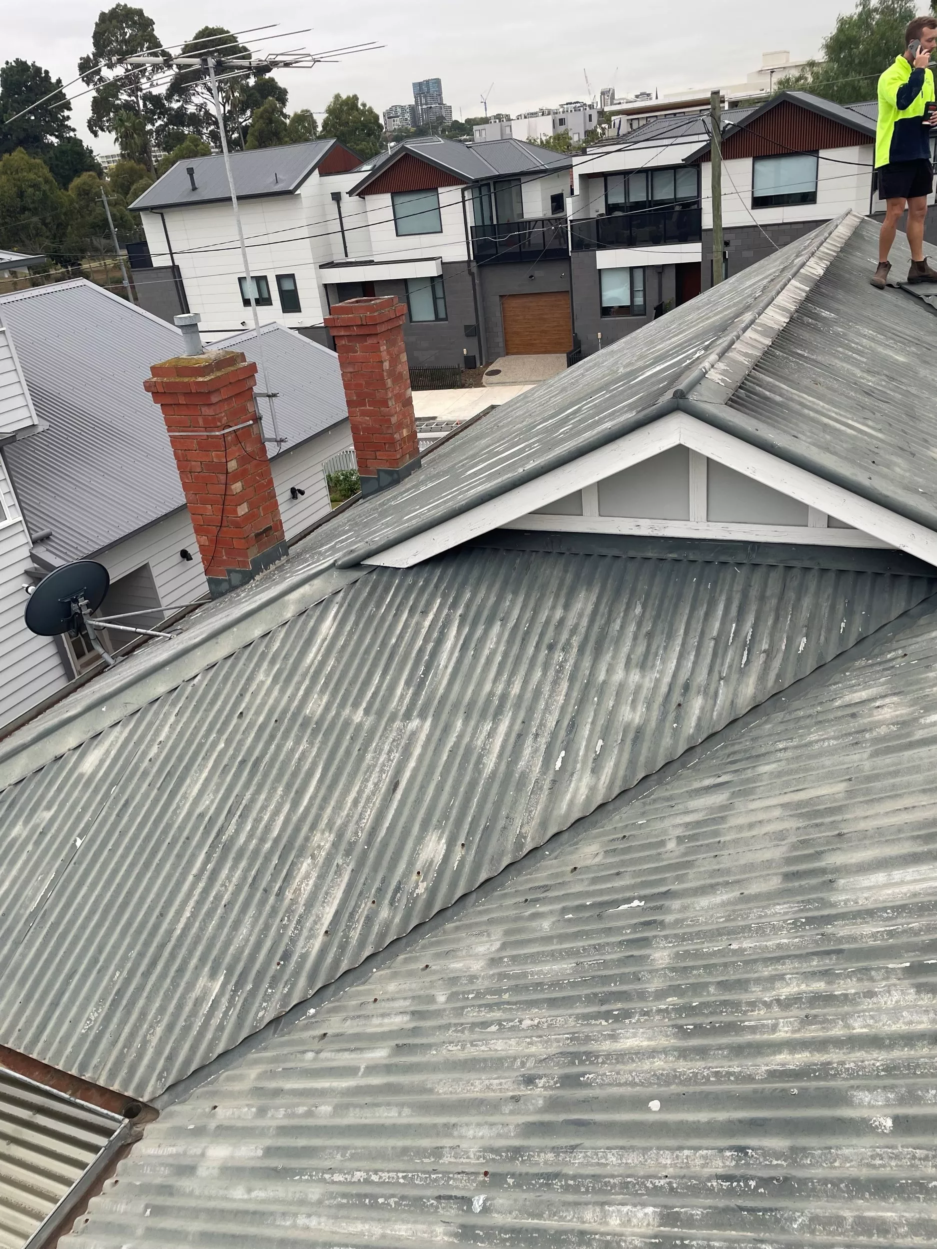 Close-up image of a gray tin roof, with surrounding houses in the background.